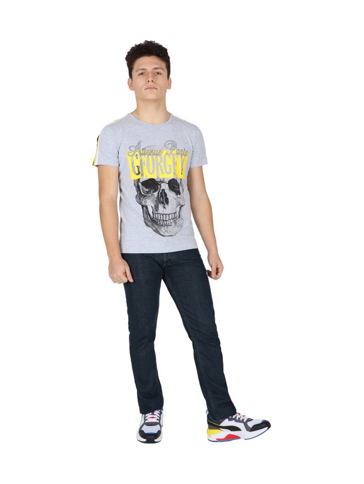 Hombre vistiendo playera gris de manga corta con estampado de calavera y letras amarillas en el pecho.