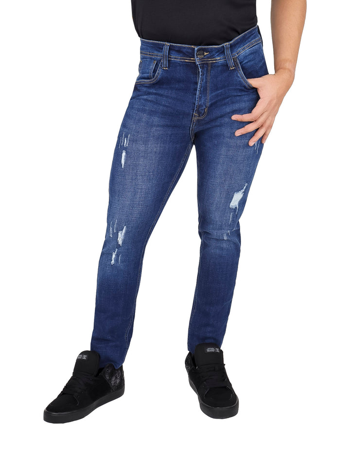 Hombre vistiendo pantalones jeans azul stone con efecto de destrucción y corte ajustado.