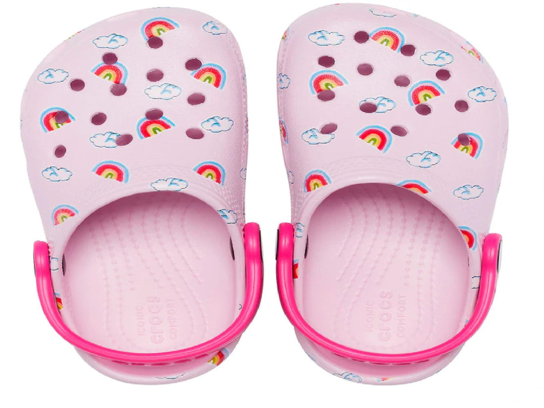 Zuecos Crocs color rosa para niña con diseño de arcoíris y nubes y correa rosa fuerte.