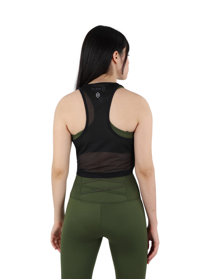Mujer vistiendo un top crop deportivo negro perforado y leggings verde oliva sobre fondo blanco.