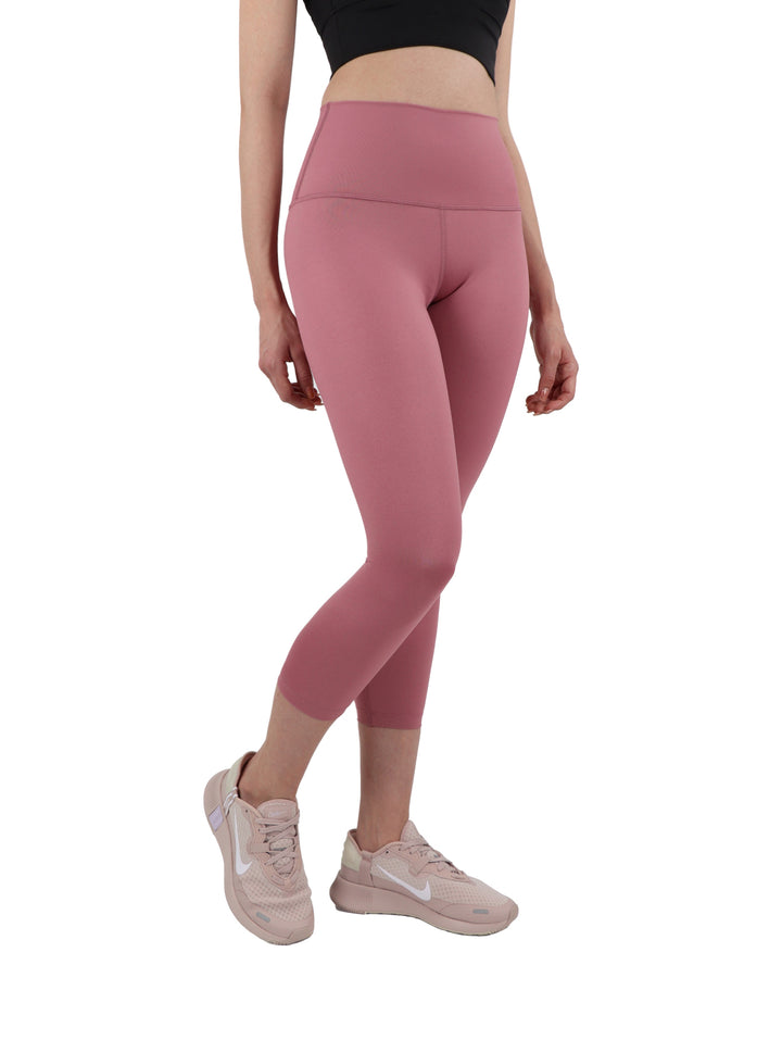 Mujer vistiendo leggings capri color rosa ajustados y tenis rosas sobre fondo blanco.