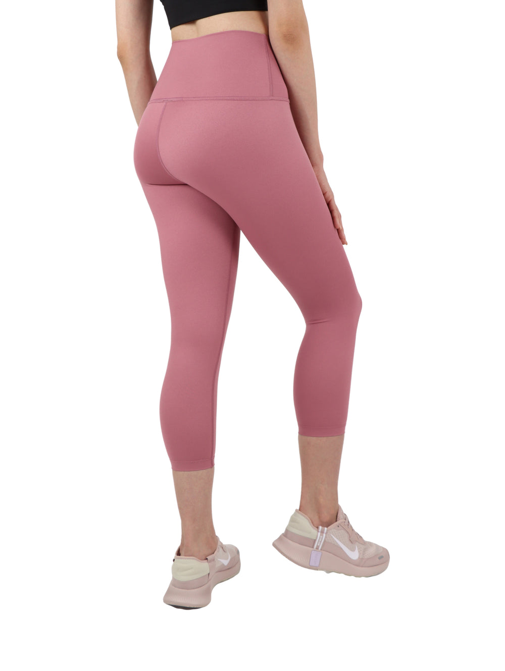 Mujer vistiendo leggings capri color rosa ajustados y tenis rosas sobre fondo blanco.