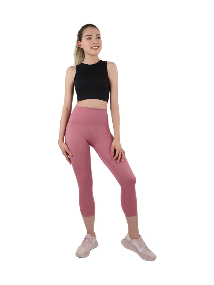 Mujer vistiendo leggings capri color rosa ajustados y tenis rosas sobre fondo blanco.