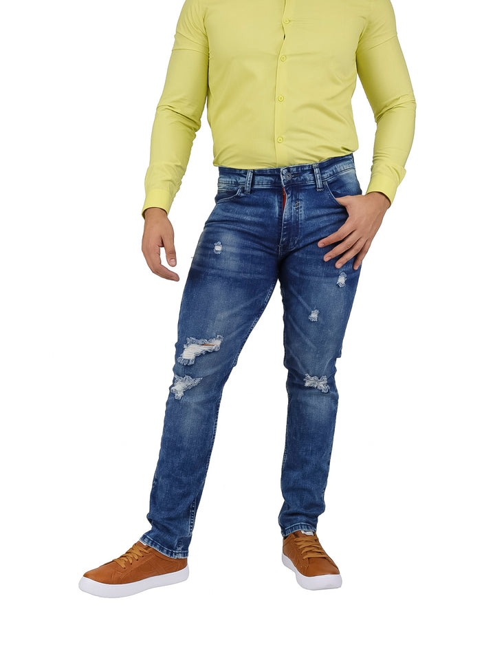 Hombre vistiendo pantalones jeans slim fit color azul con detalles de desgaste y roturas frontales.