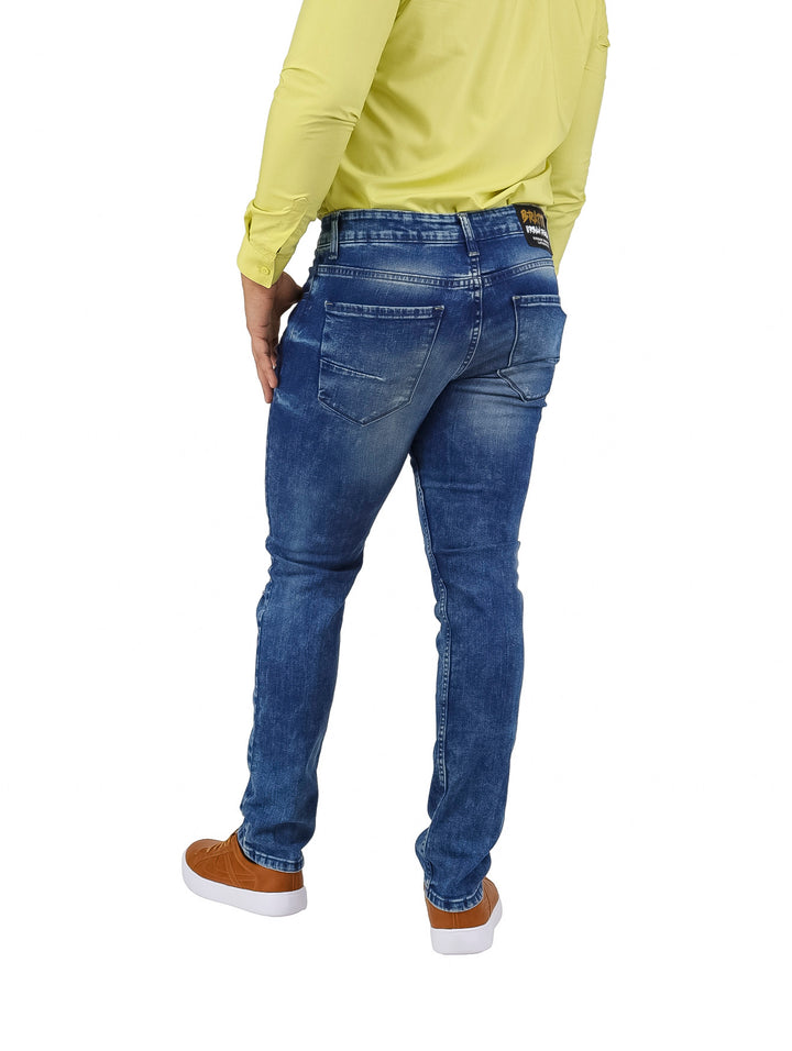 Hombre vistiendo pantalones jeans slim fit color azul con detalles de desgaste y roturas frontales.