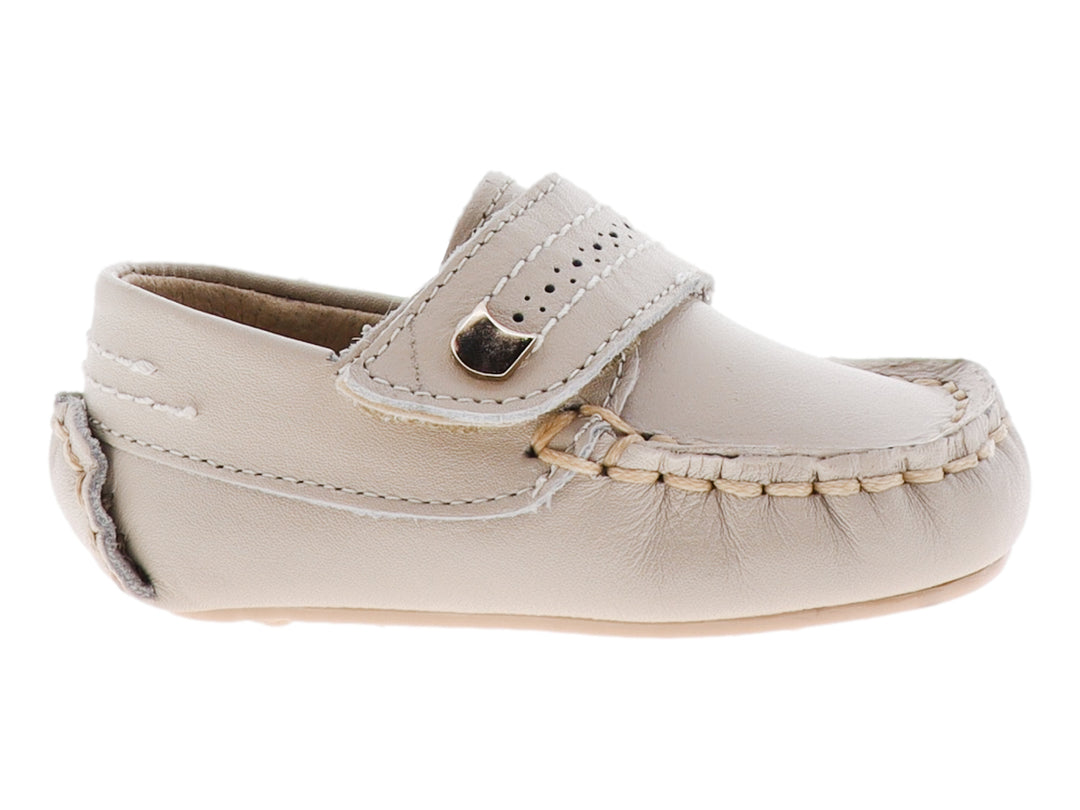 Zapato tipo mocasín para bebé en color hueso con correa ajustable y detalle metálico dorado.