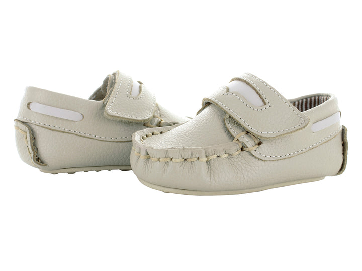 Par de zapatos mocasines color oro para bebé con cierre de correa y costuras decorativas.