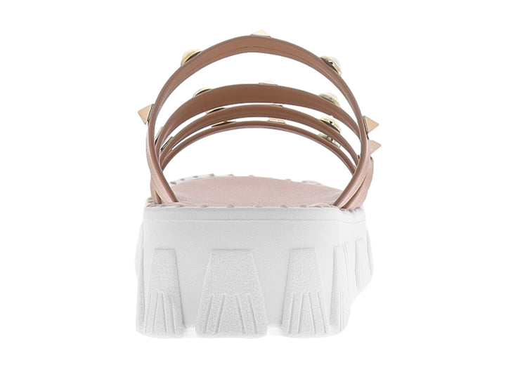 Sandalias de plataforma color maquillaje con tiras adornadas con perlas y tachuelas doradas sobre suela blanca.