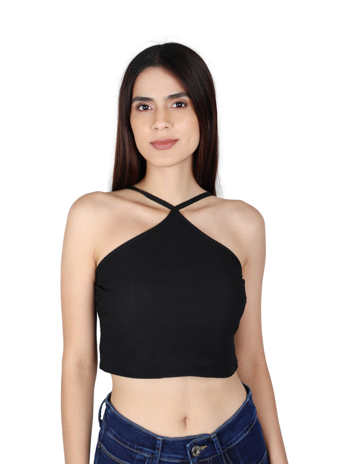 Mujer vistiendo un crop top negro de cuello halter y jeans azules sobre fondo blanco.