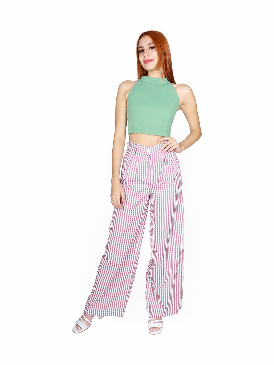 Mujer vistiendo un crop top color verde sage con cuello halter y pantalones a cuadros rosas.