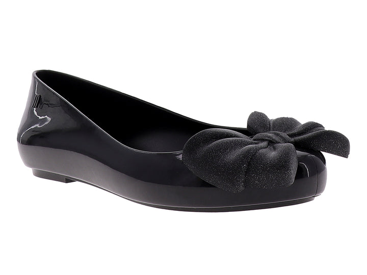 Zapato plano color negro brillante con un moño decorativo en la parte frontal.