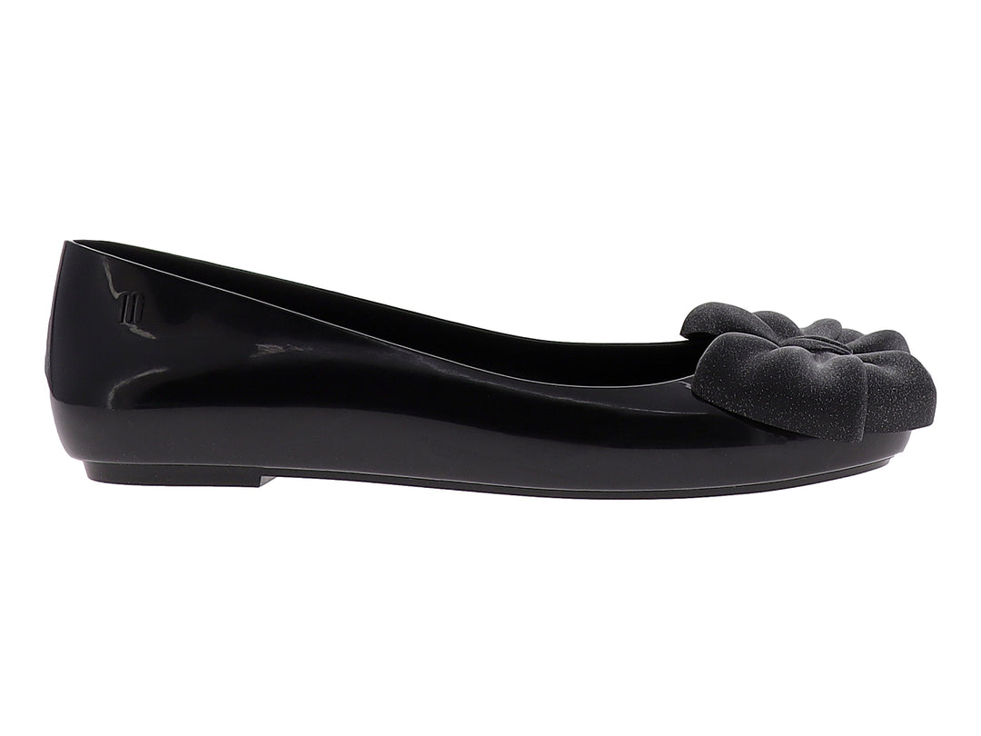 Zapato plano color negro brillante con un moño decorativo en la parte frontal.