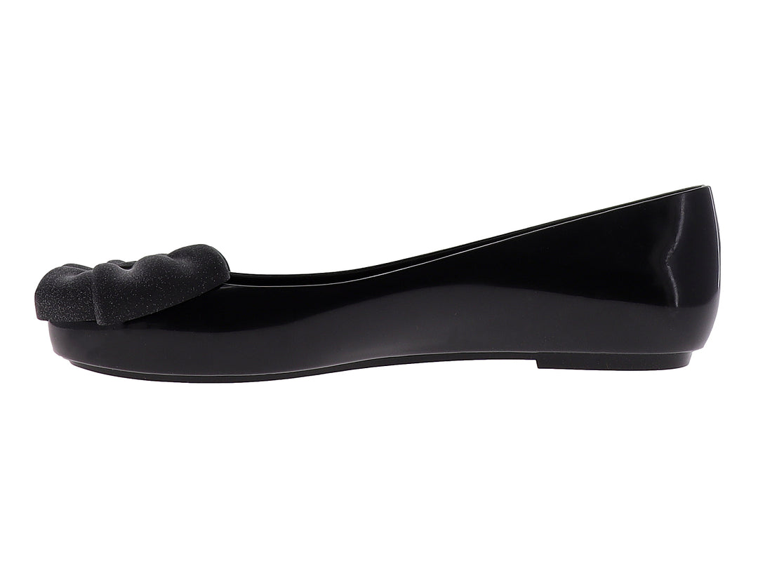 Zapato plano color negro brillante con un moño decorativo en la parte frontal.