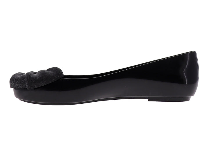 Zapato plano color negro brillante con un moño decorativo en la parte frontal.
