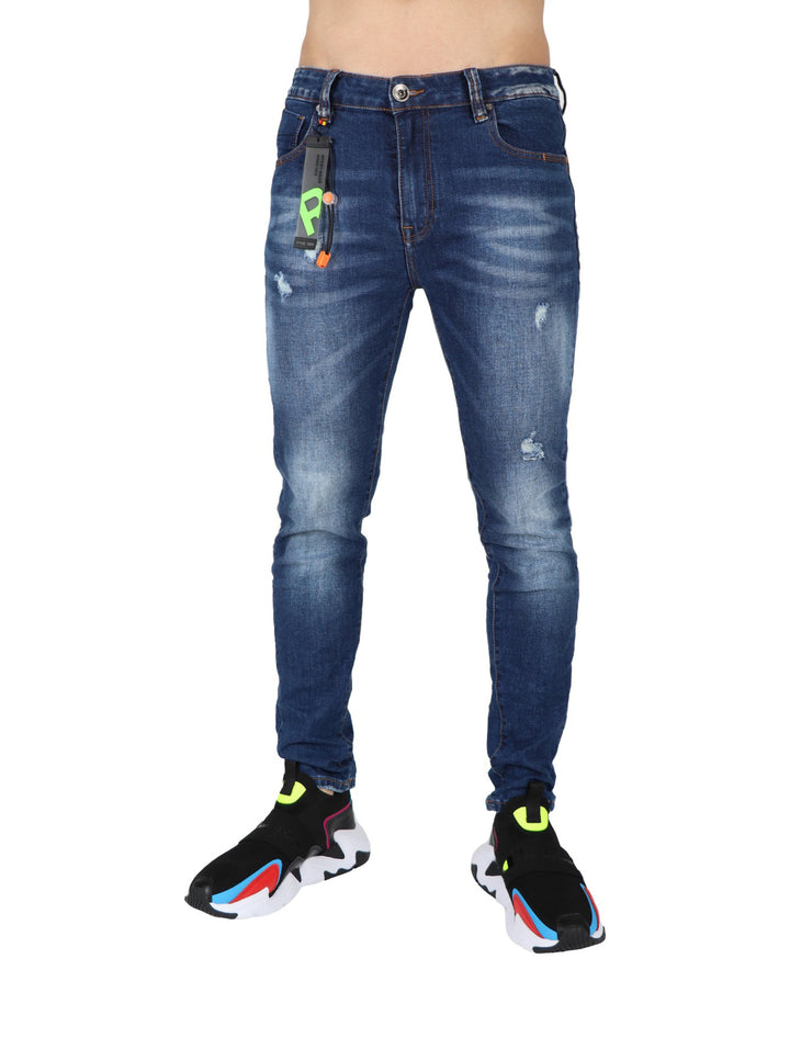 Hombre modelando pantalón de mezclilla azul ajustado con camiseta negra y calzado deportivo.
