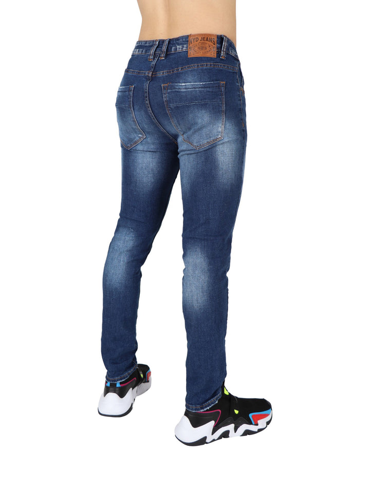 Hombre modelando pantalón de mezclilla azul ajustado con camiseta negra y calzado deportivo.