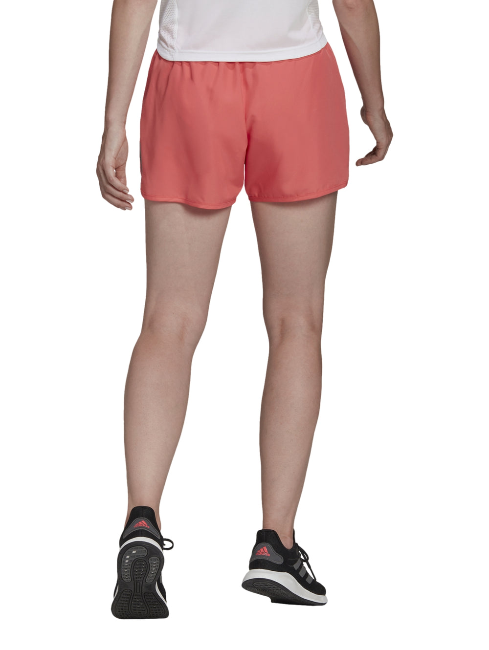 Mujer vistiendo shorts deportivos Adidas color coral para correr sobre fondo blanco.