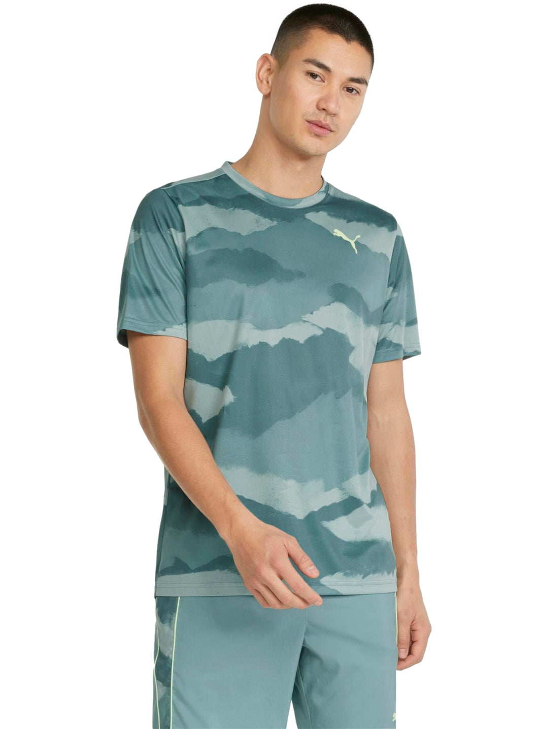 Hombre vistiendo camiseta deportiva PUMA color mineral blue con estampado abstracto en tonos azules y verdes.