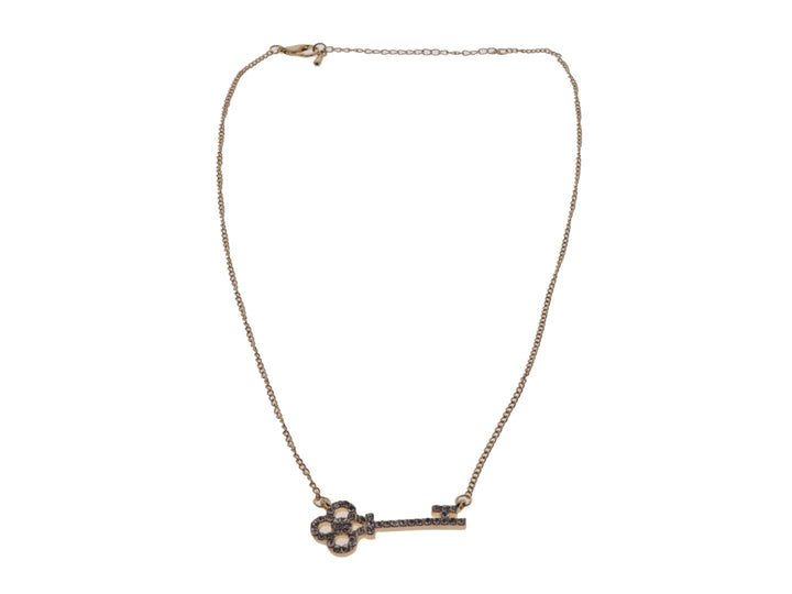 Collar dorado con cadena delgada y dije en forma de llave adornado con cristales oscuros.