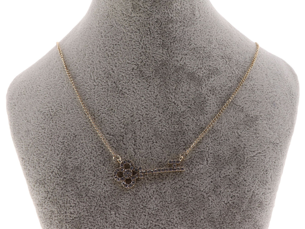 Collar dorado con cadena delgada y dije en forma de llave adornado con cristales oscuros.