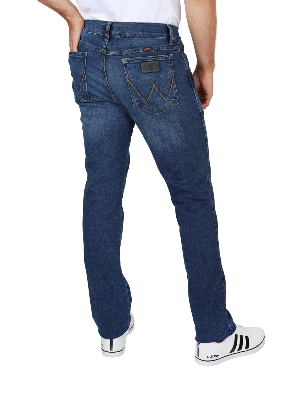 Hombre vistiendo pantalones Wrangler de color índigo y tenis blancos.