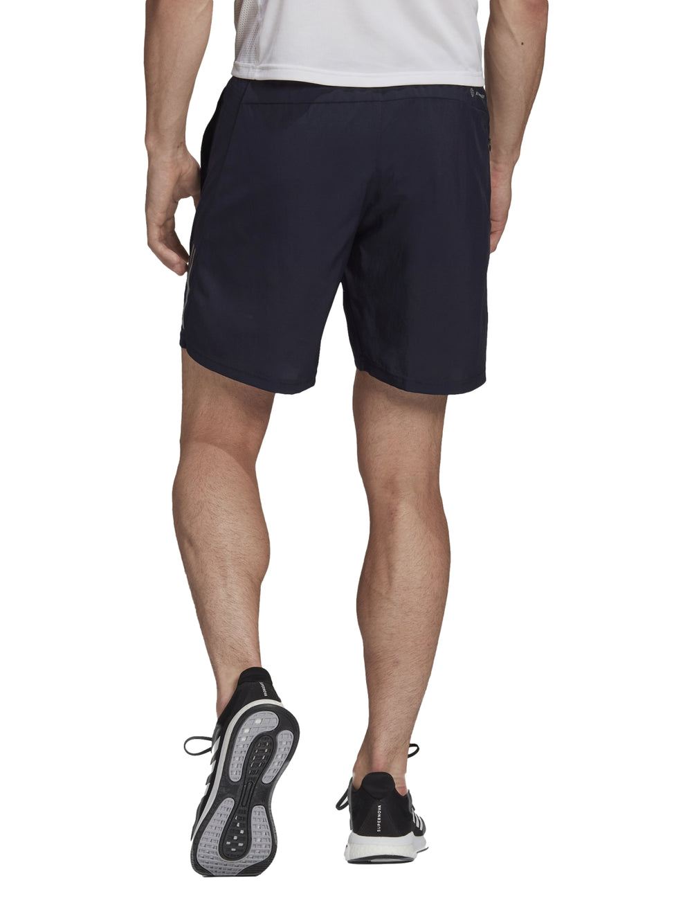 Hombre vistiendo shorts deportivos Adidas color azul marino Legend Ink con detalles laterales reflectantes.