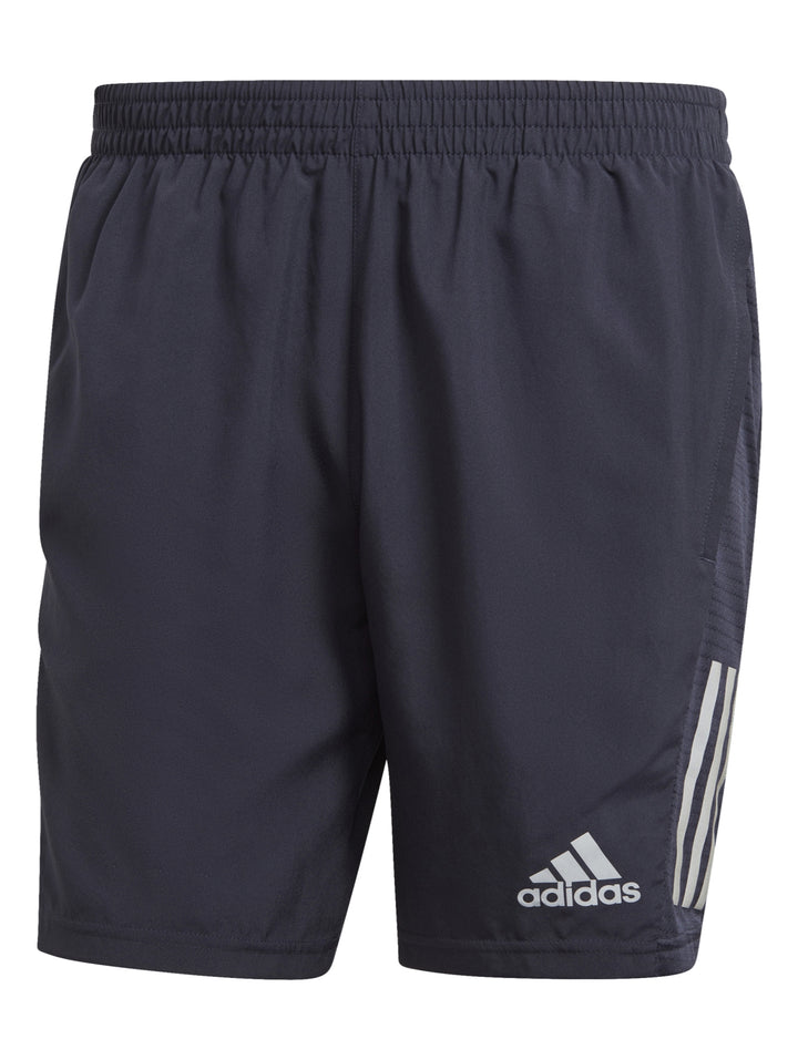 Hombre vistiendo shorts deportivos Adidas color azul marino Legend Ink con detalles laterales reflectantes.