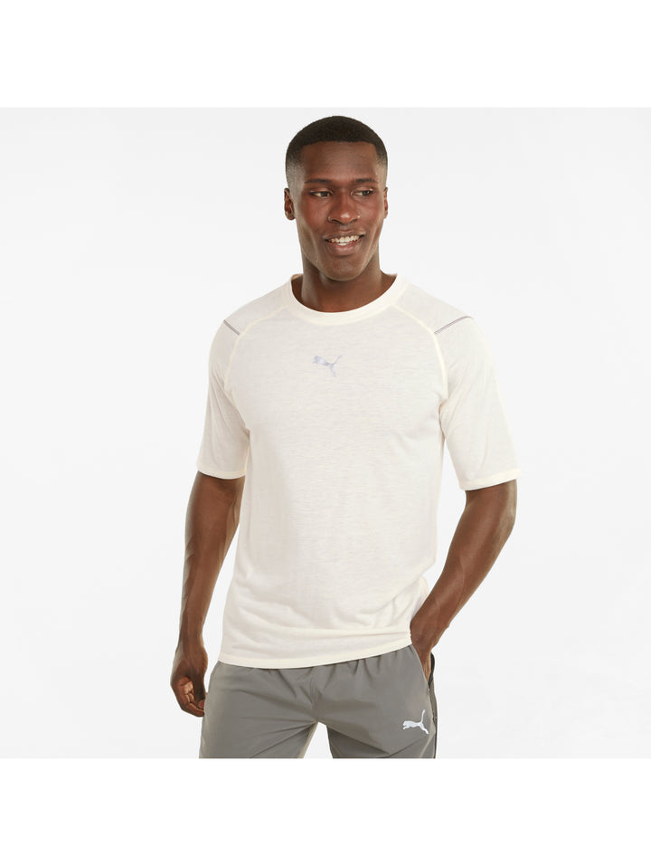 Hombre vistiendo camiseta deportiva PUMA de color marfil y shorts grises sobre fondo blanco.