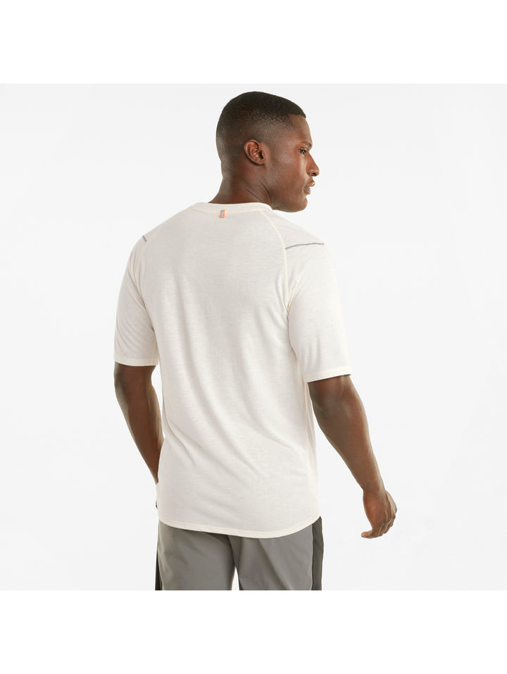 Hombre vistiendo camiseta deportiva PUMA de color marfil y shorts grises sobre fondo blanco.