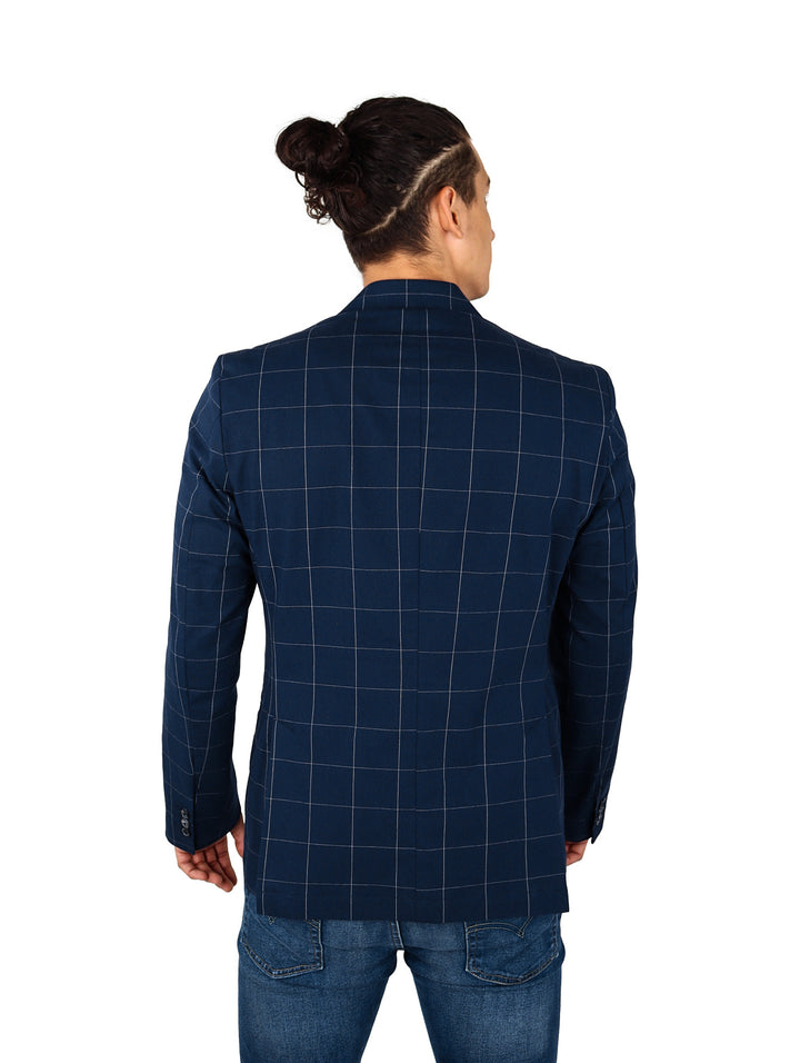 Hombre vistiendo un saco color marino con estampado de cuadros, playera roja y jeans azules.