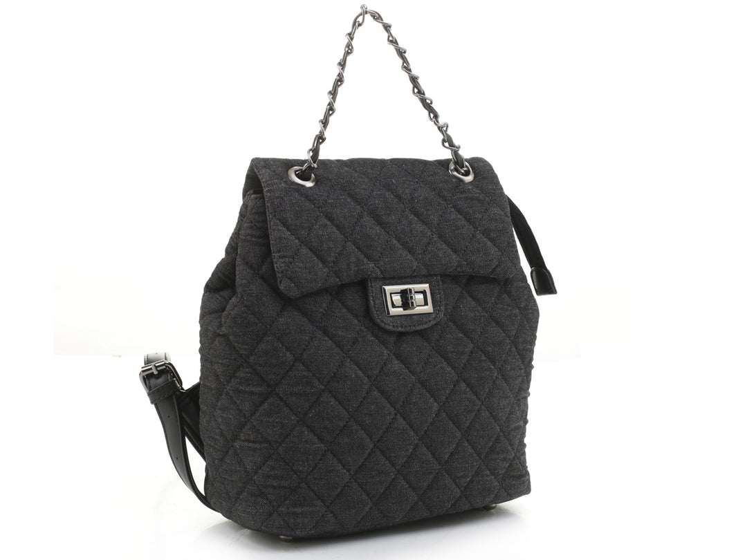 Mochila negra acolchada con asa de cadena plateada y cierre de broche metálico.