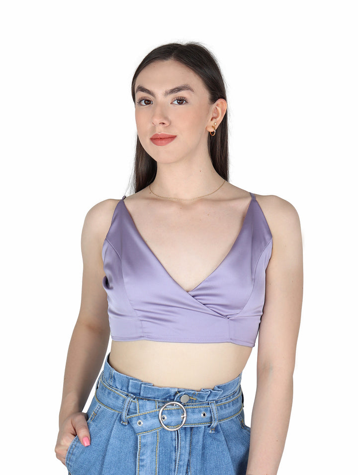 Mujer vistiendo un crop top color lavanda de tirantes con acabado satinado y pantalones vaqueros azules.