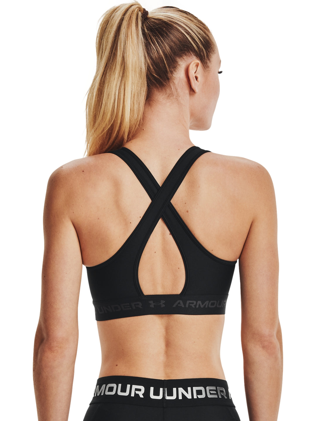 Mujer vistiendo un top deportivo Under Armour color negro con banda elástica gris en la base.