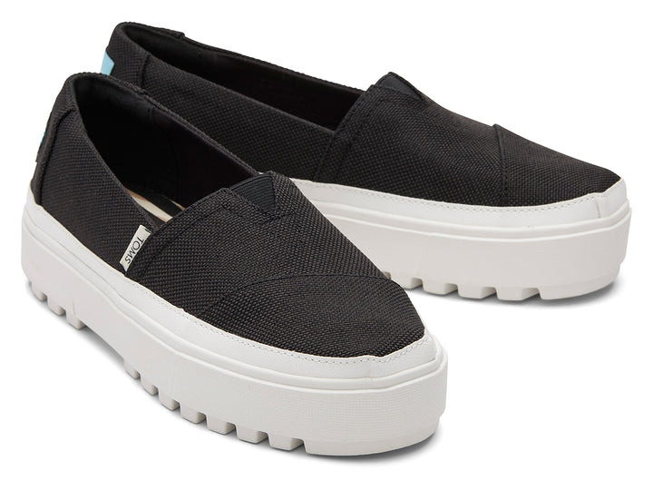 Zapatos slip-on TOMS color negro con suela blanca de plataforma gruesa.