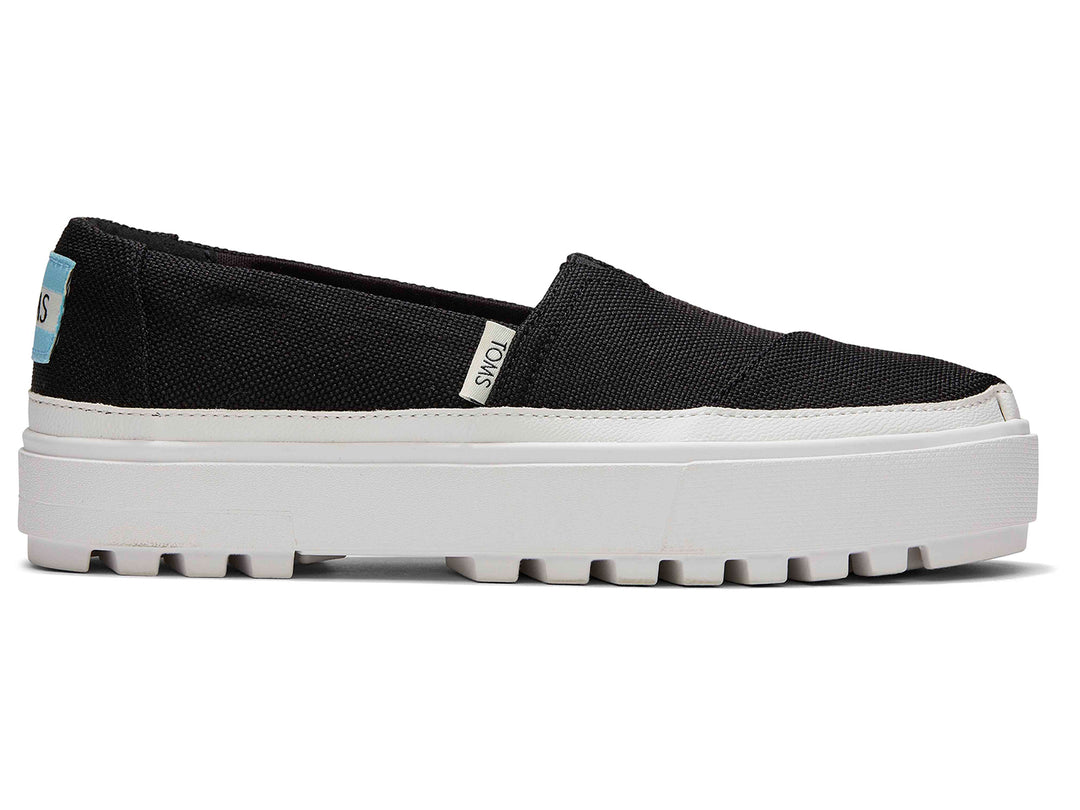 Zapatos slip-on TOMS color negro con suela blanca de plataforma gruesa.
