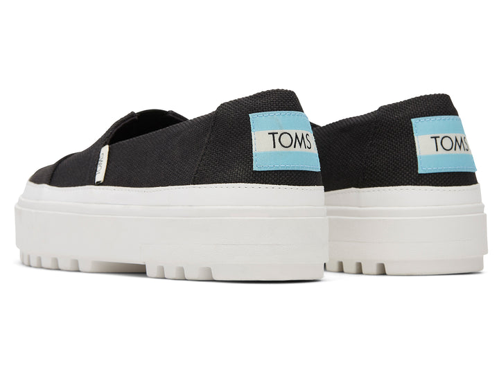 Zapatos slip-on TOMS color negro con suela blanca de plataforma gruesa.