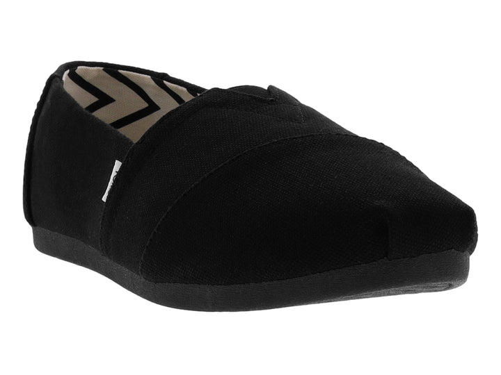 Zapato slip-on TOMS de color negro en tela de algodón reciclado con suela plana.