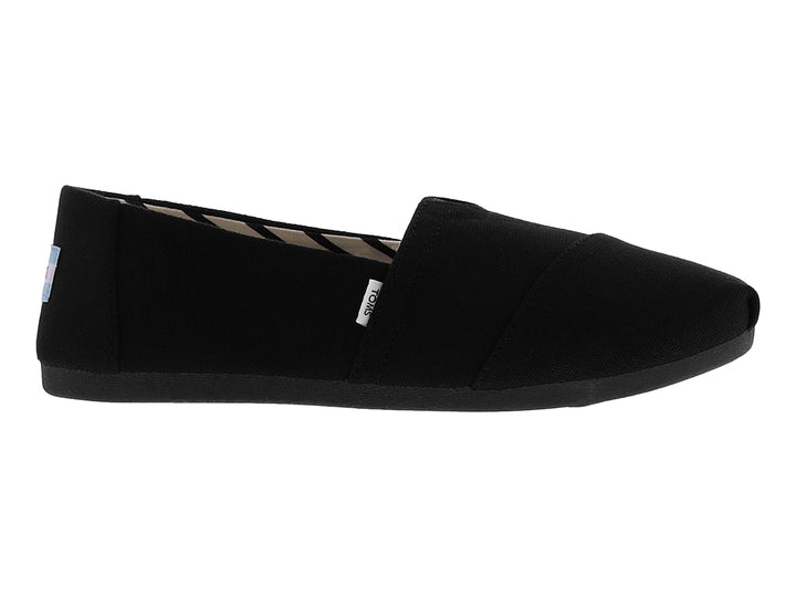 Zapato slip-on TOMS de color negro en tela de algodón reciclado con suela plana.