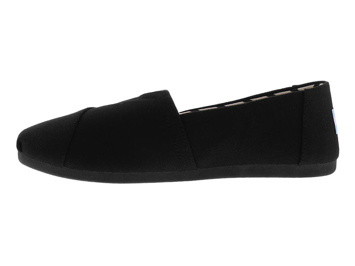 Zapato slip-on TOMS de color negro en tela de algodón reciclado con suela plana.