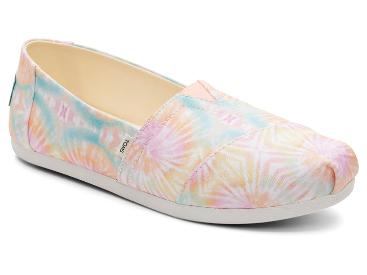 Zapato TOMS estilo slip-on de tela con estampado tie dye en tonos rosa, amarillo y azul con suela blanca.