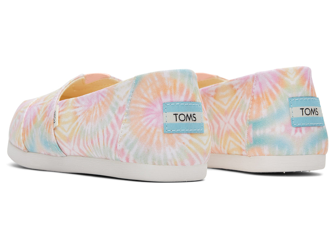 Zapato TOMS estilo slip-on de tela con estampado tie dye en tonos rosa, amarillo y azul con suela blanca.