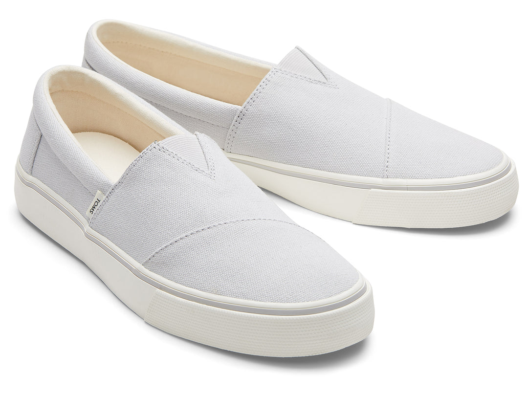 Par de zapatos planos TOMS de color gris claro con suela blanca, estilo slip-on.