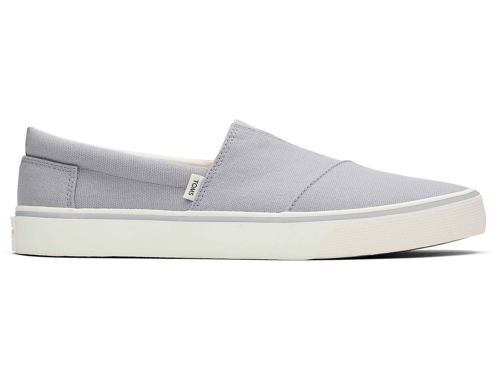 Par de zapatos planos TOMS de color gris claro con suela blanca, estilo slip-on.