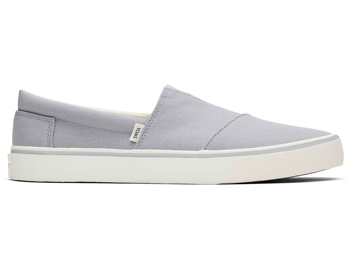 Par de zapatos planos TOMS de color gris claro con suela blanca, estilo slip-on.