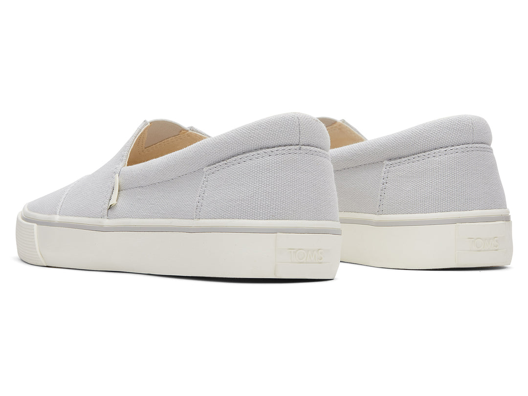 Par de zapatos planos TOMS de color gris claro con suela blanca, estilo slip-on.