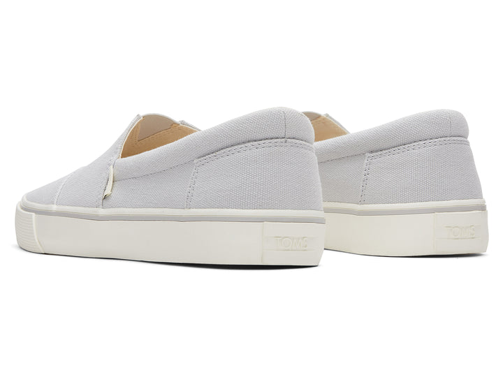 Par de zapatos planos TOMS de color gris claro con suela blanca, estilo slip-on.