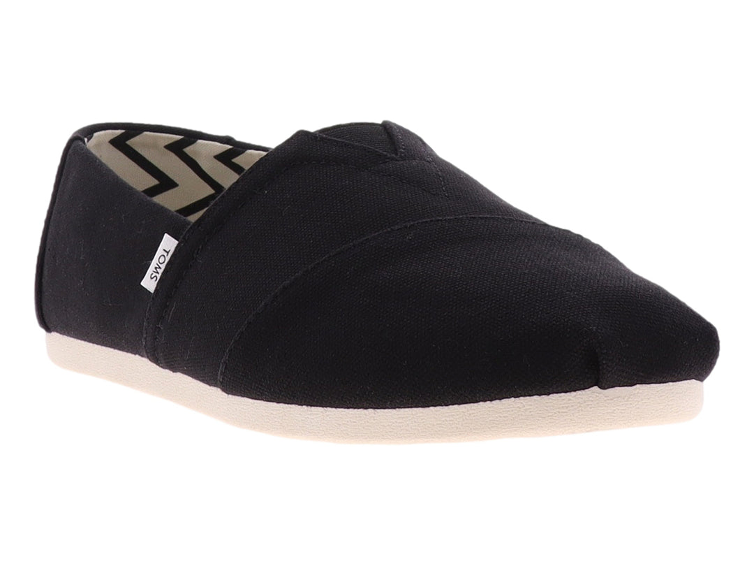 Zapato plano slip-on TOMS de tela negra con suela blanca.