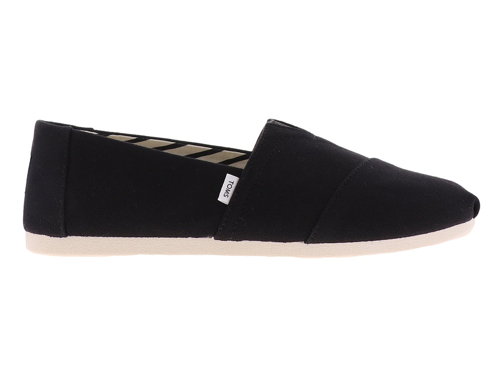 Zapato plano slip-on TOMS de tela negra con suela blanca.