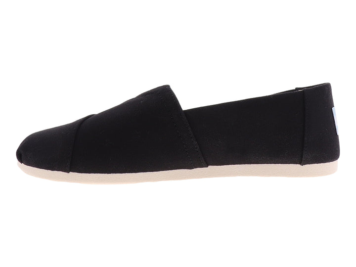Zapato plano slip-on TOMS de tela negra con suela blanca.