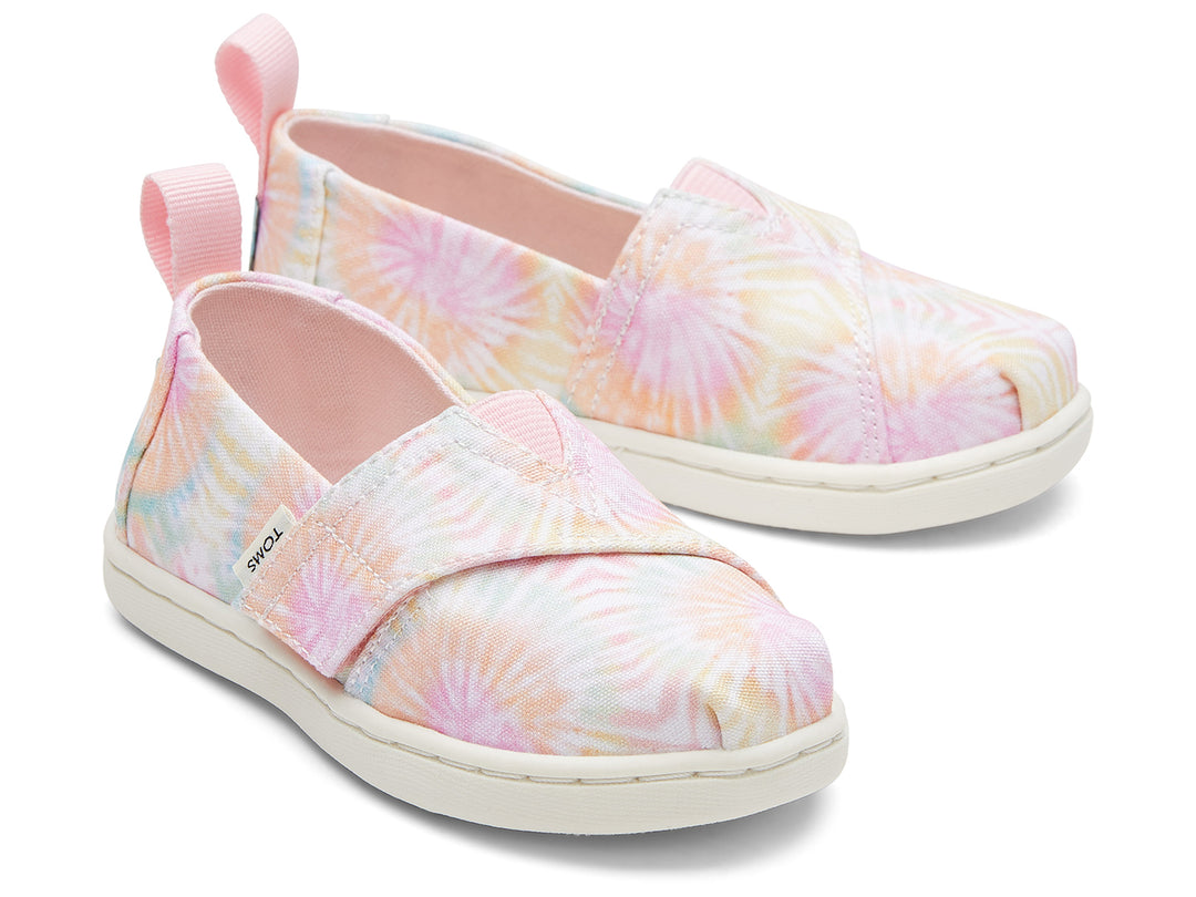 Par de zapatos TOMS estilo slip-on con estampado tie dye en tonos rosa, amarillo y azul con suela blanca.
